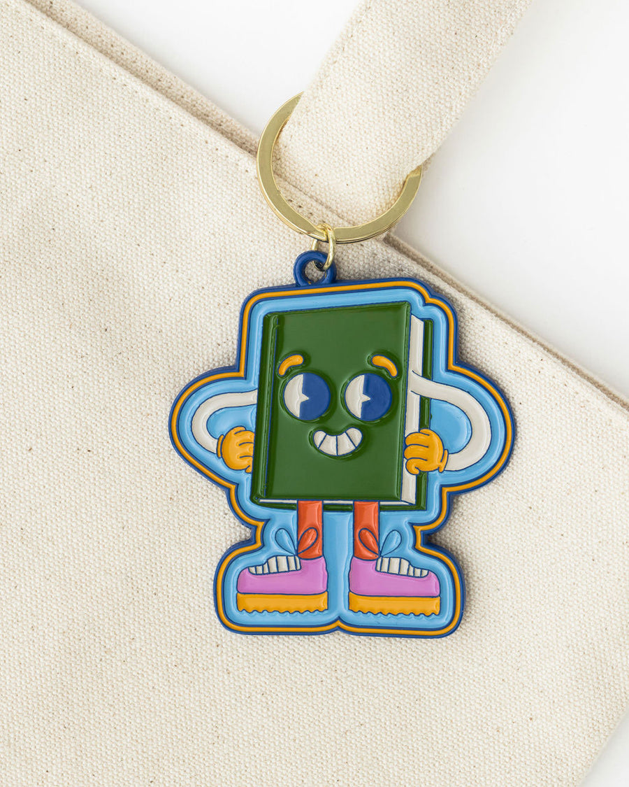 enamel keychain with green book man with arms, face and legs on bag