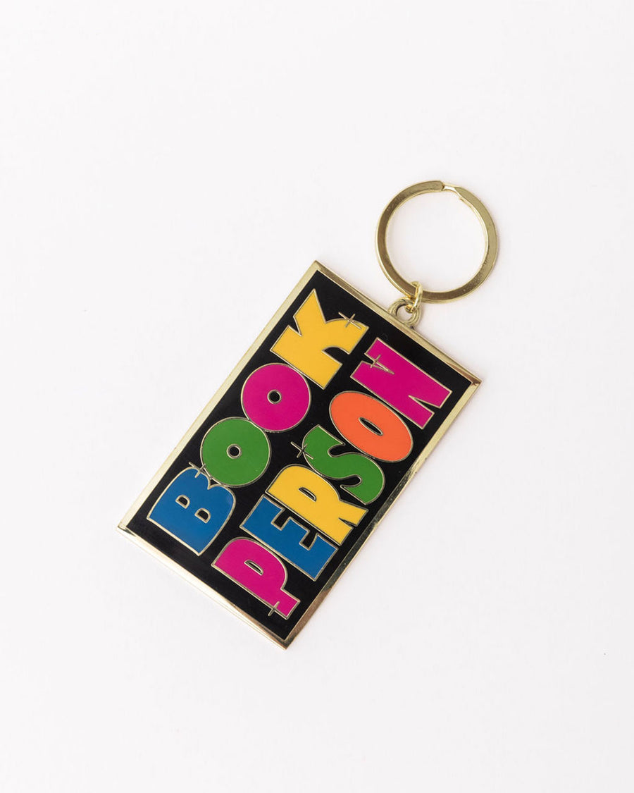 sideview of enamel keychain with black rectangle with colorful 'book person' across the front