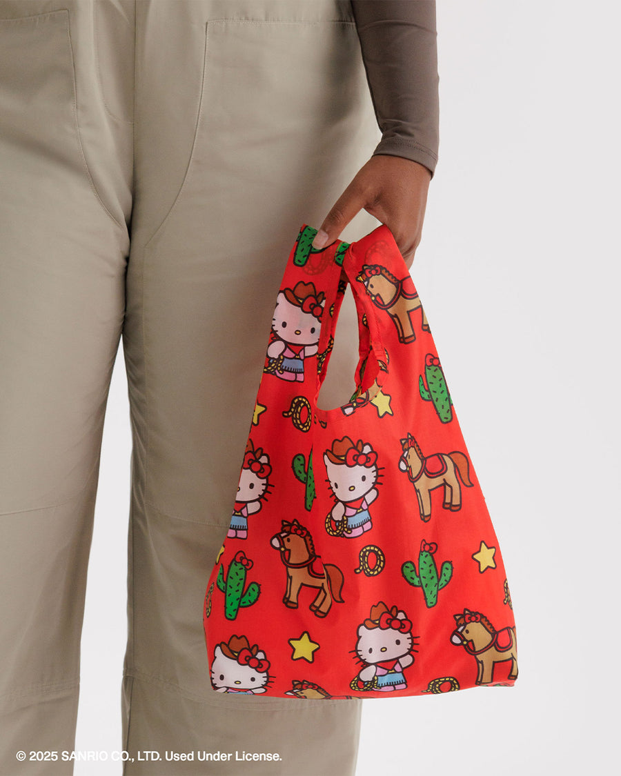 model holding coral baby baggu with hello kitty dressed like a cowboy and has horse, cactus, lassos, and stars surrounding