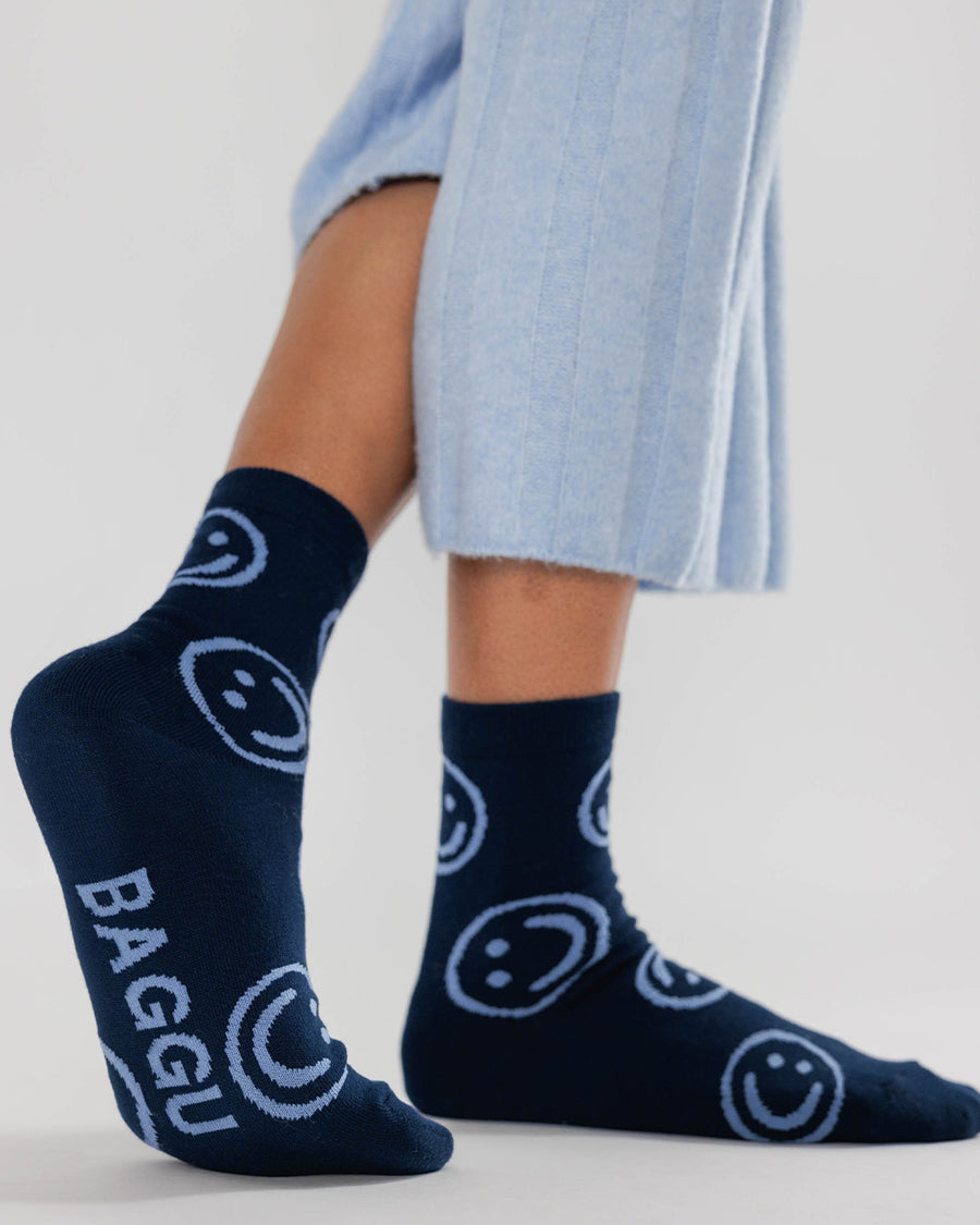 model wearing dark navy baggu socks with light blue smiley faces