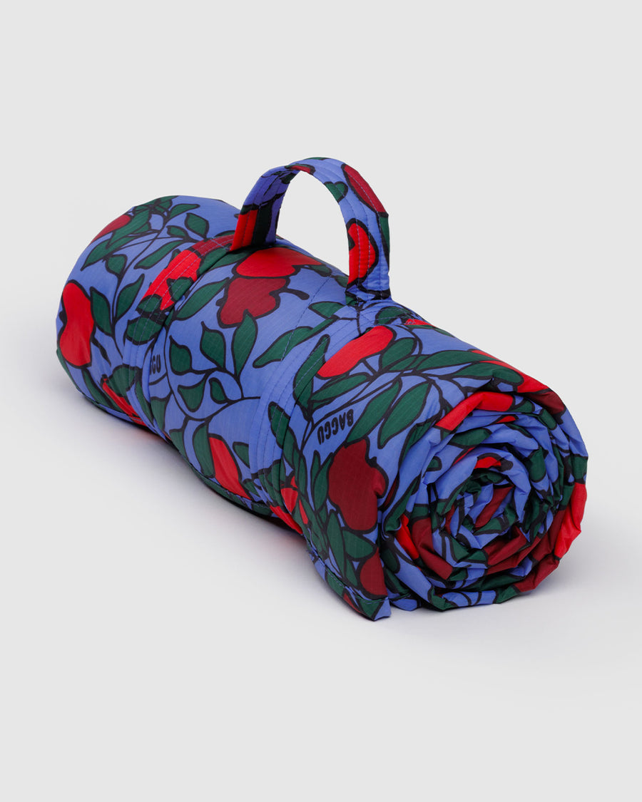 rolled blue puffy picnic blanket with strap with handle and apple tree print