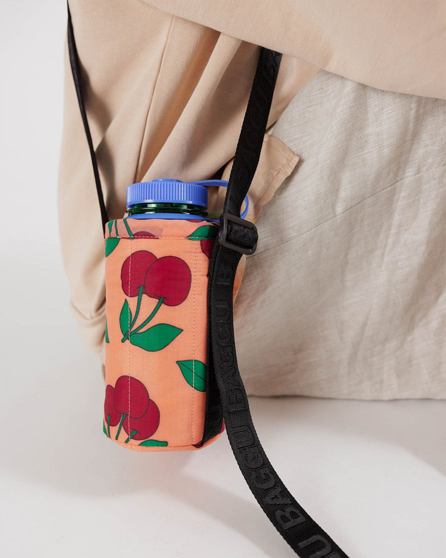 up close of model wearing peach puffy water bottle sling with cherry print