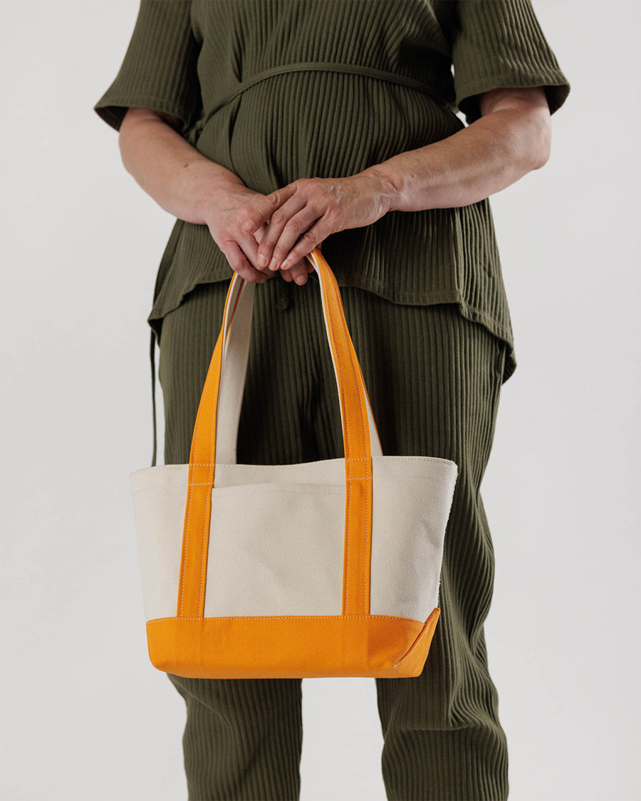 model holding tan small boat tote with tangerine accents