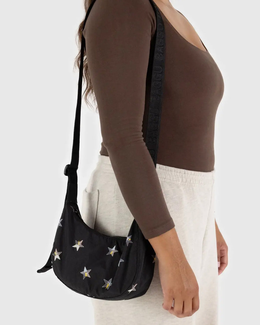 up close of model wearing black small nylon crescent bag with silver holographic stars