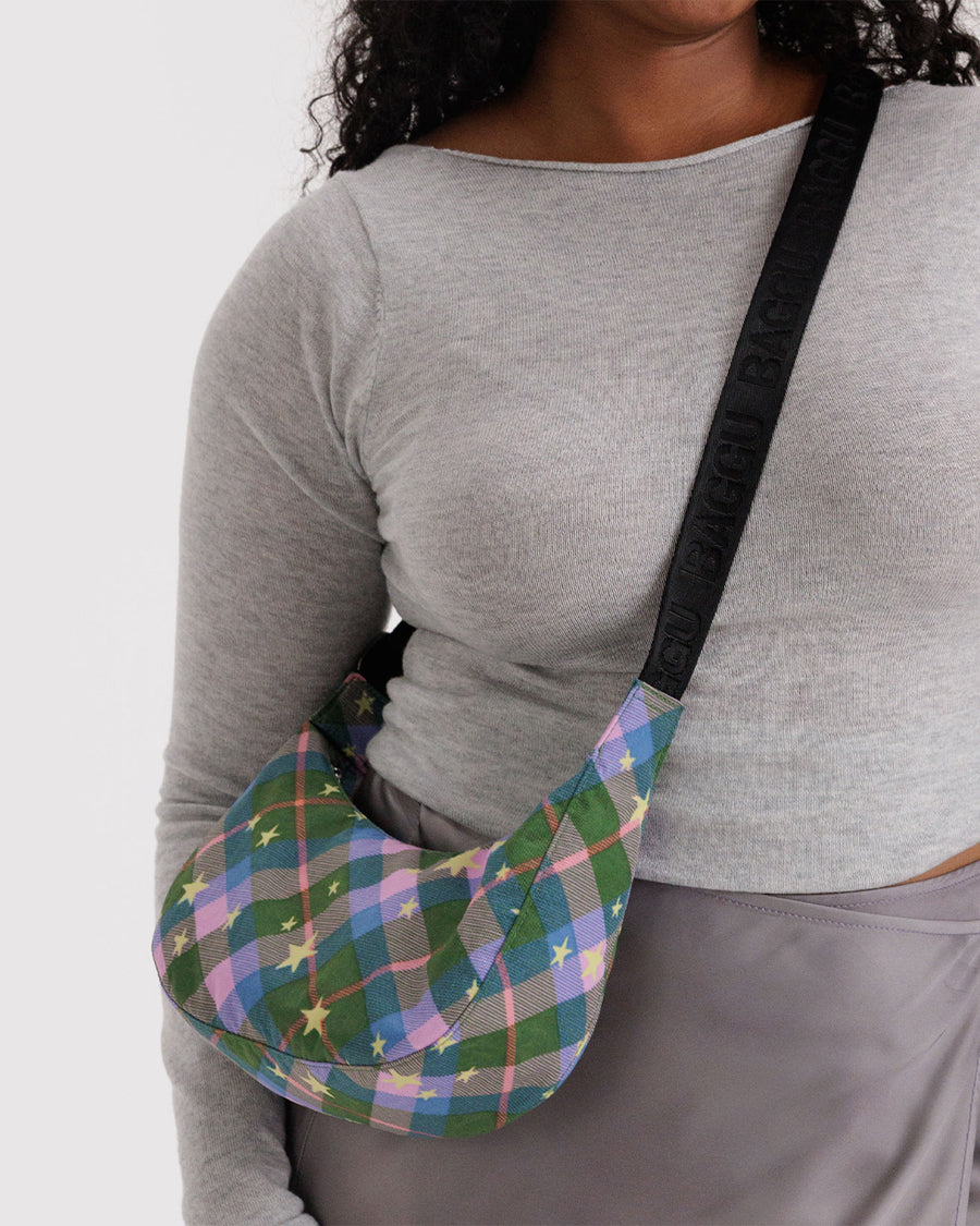 model carrying pink, green and blue plaid small crescent bag with black adjustable strap