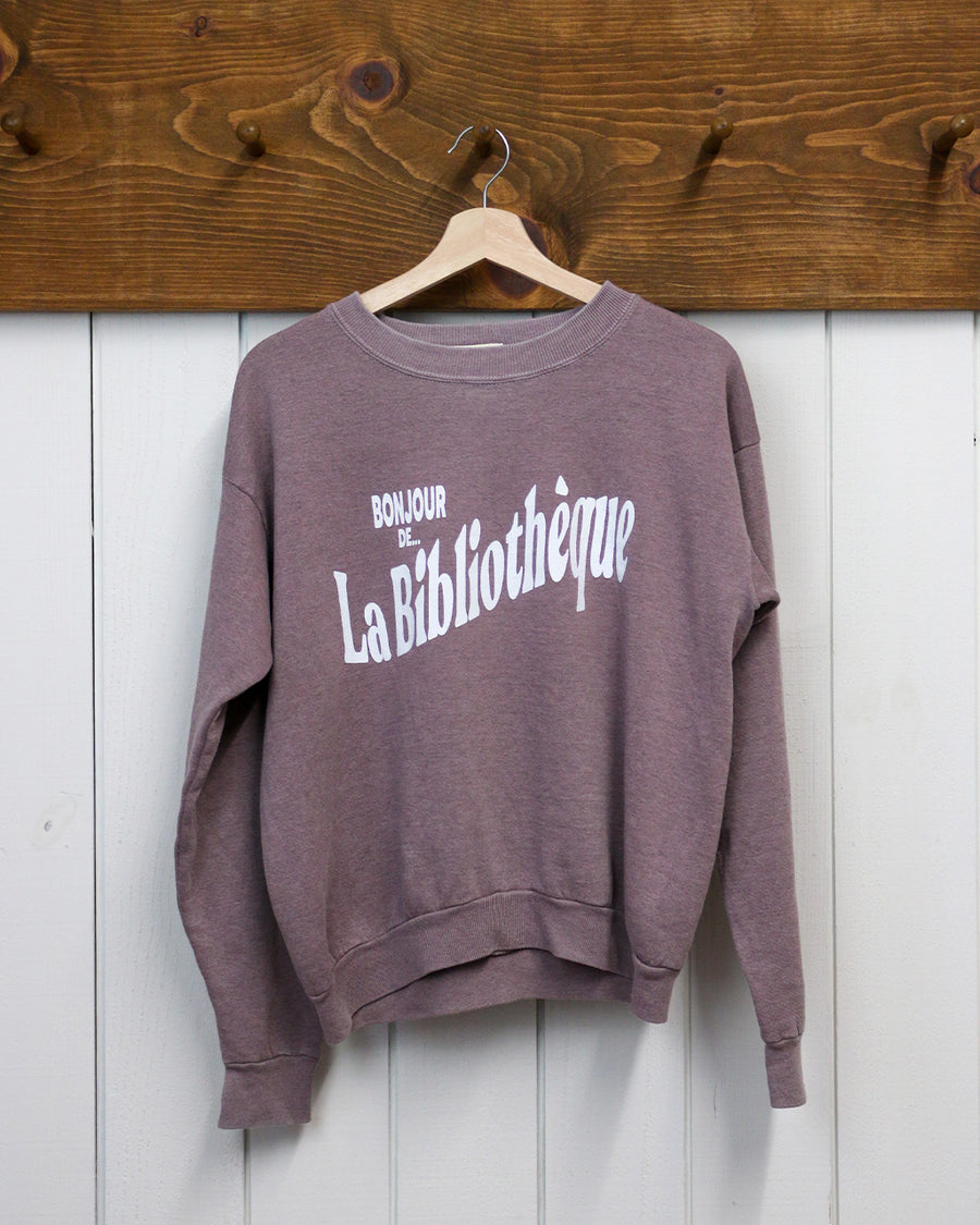 rosewood sweatshirt with white Bonjour De La Bibliothèque across the front hanging on a hanger