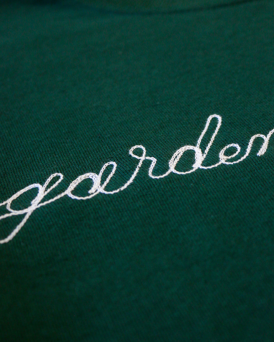up close of dark green sweatshirt with white chainstitch garden enthusiast across the front