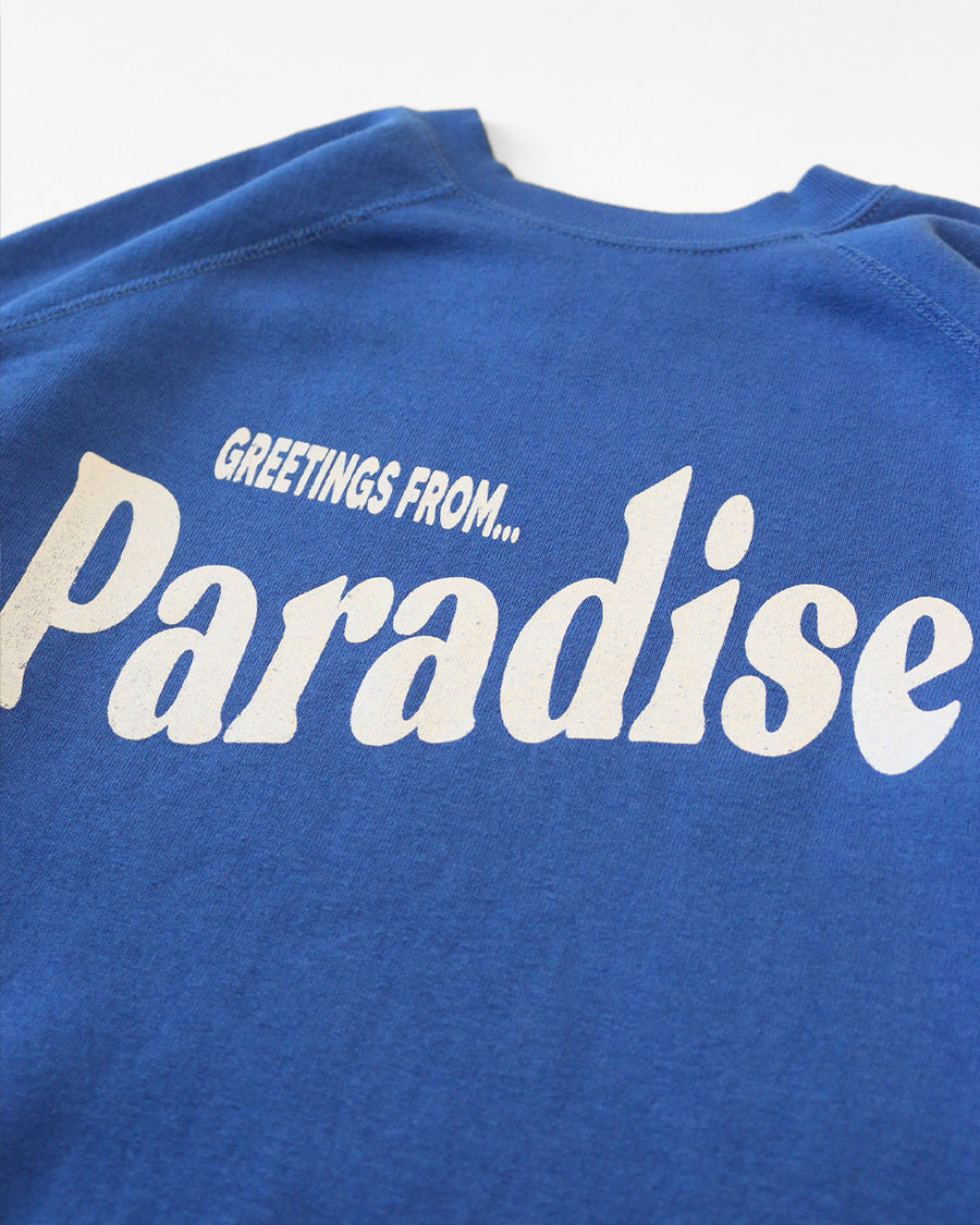 up close of blue sweatshirt with white 'GREETING FROM...PARADISE' across the front