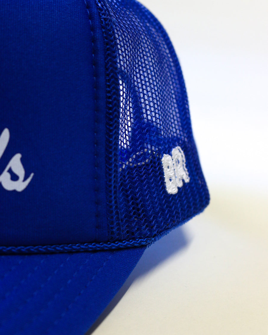 side view of royal blue trucker hat with white 'HOTEL du BEST REGARDS' across the front