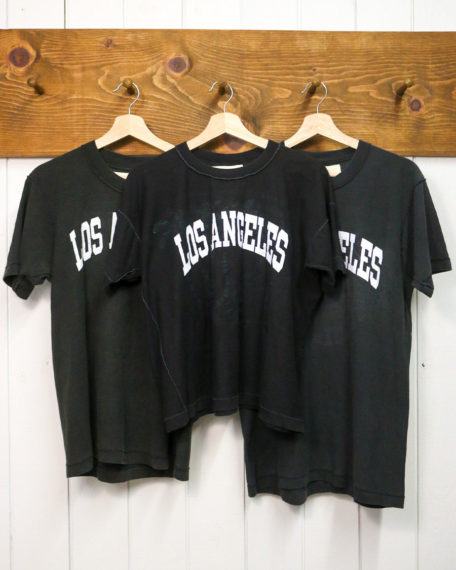 three hanging black upcycled tees with white LOS ANGELES across the front