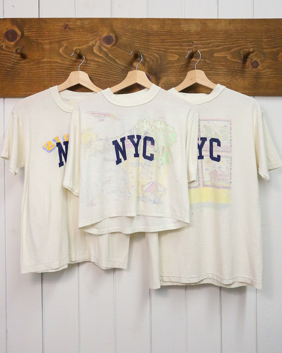 three hanging white upcycled tees with navy NYC across the front