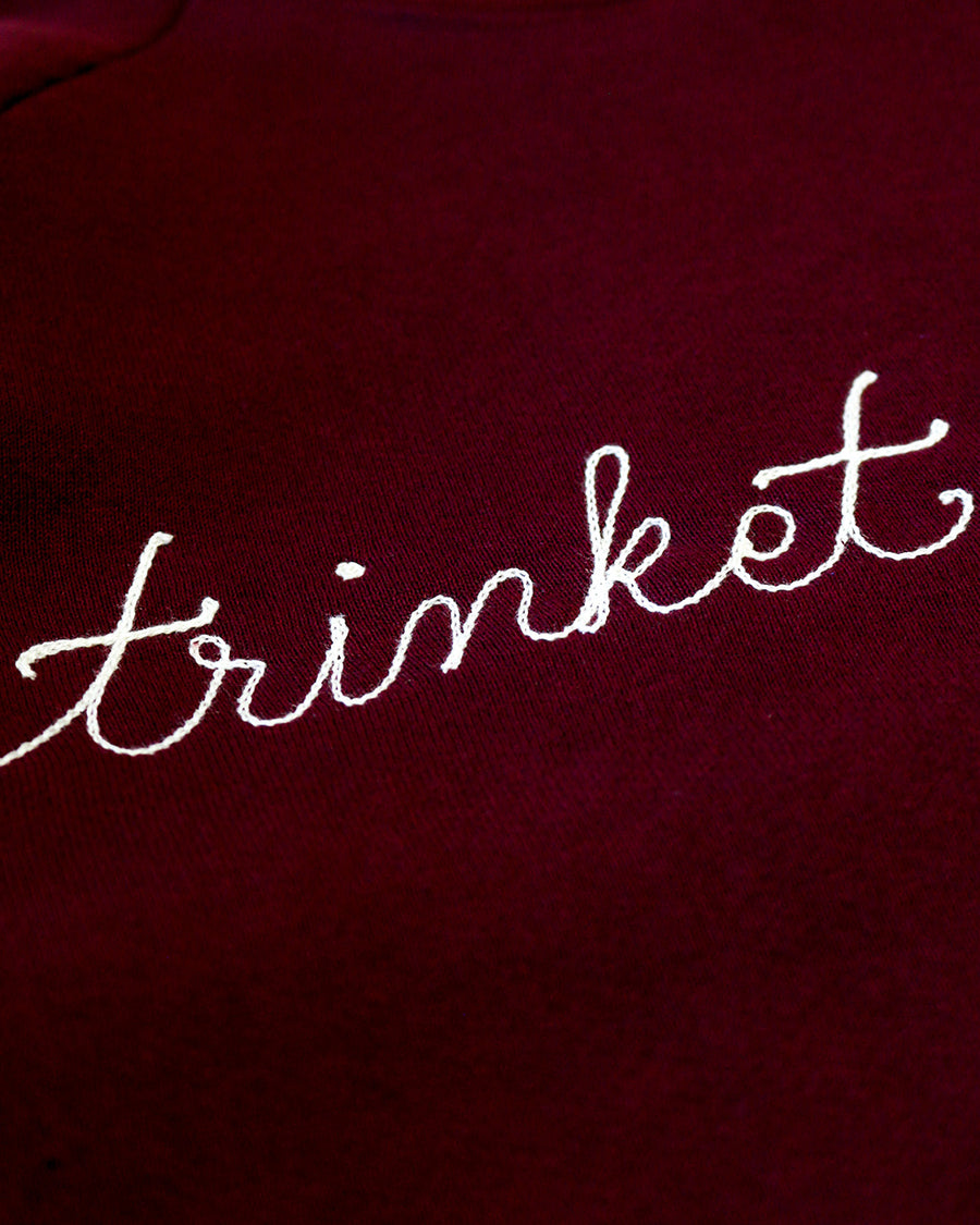 up close of maroon sweatshirt with white chainstitch trinket collector across the front