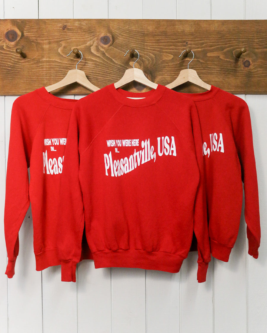 red sweatshirt with white 'WISH YOU WERE HERE IN...PLEASANTVILLE, USA' across the front hanging on a hanger