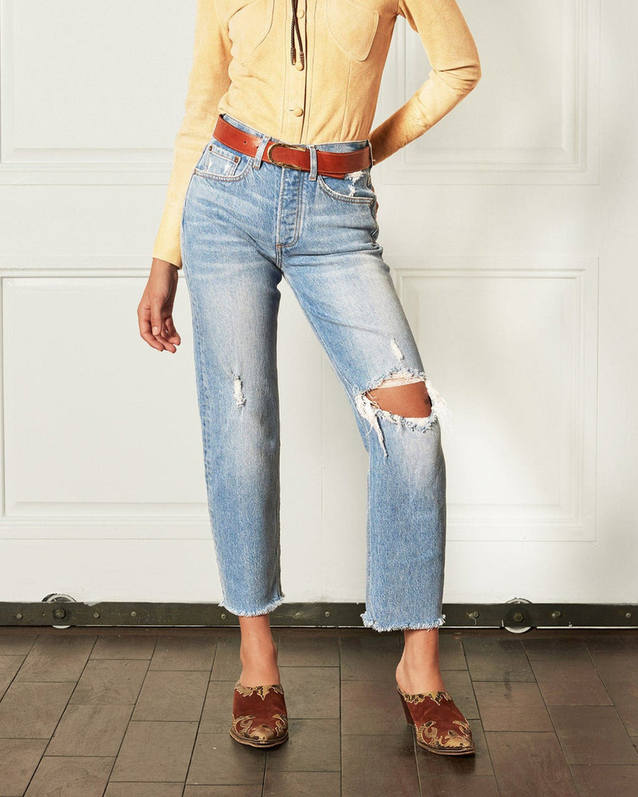 front view of model wearing light denim jeans with raw hem and distressing throughout
