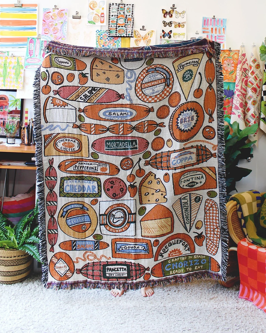model holding white tapestry blankets with all over meat and cheese print and fringe edges