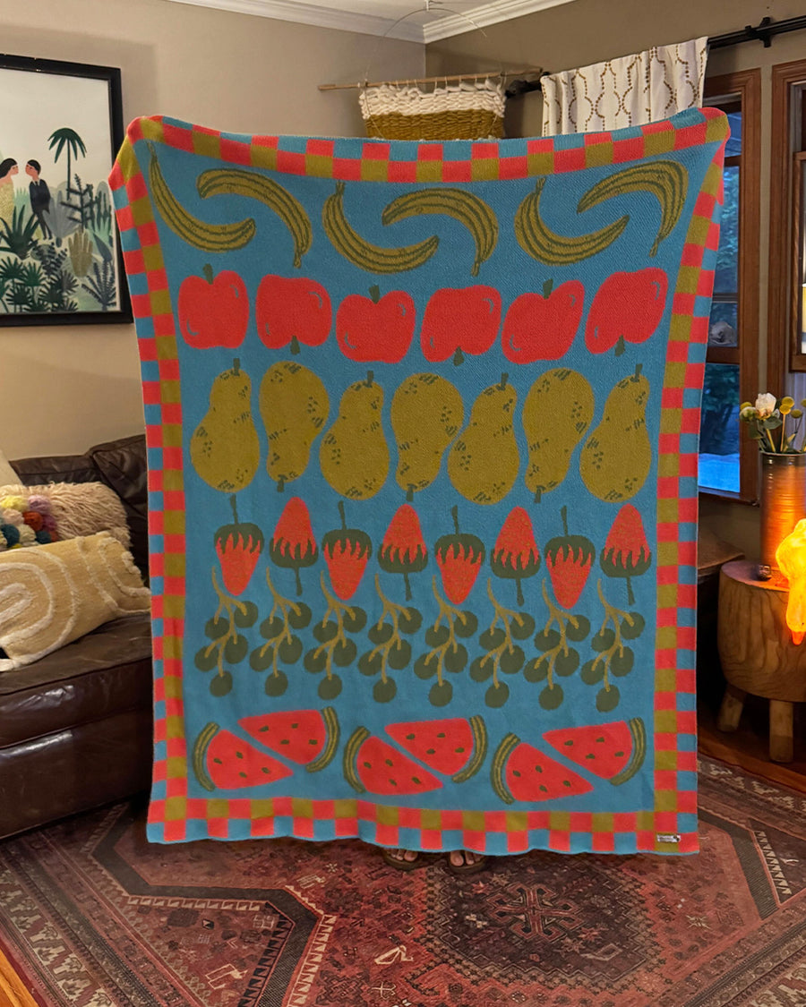 aqua throw blanket with checkered border and various colorful fruits in a line