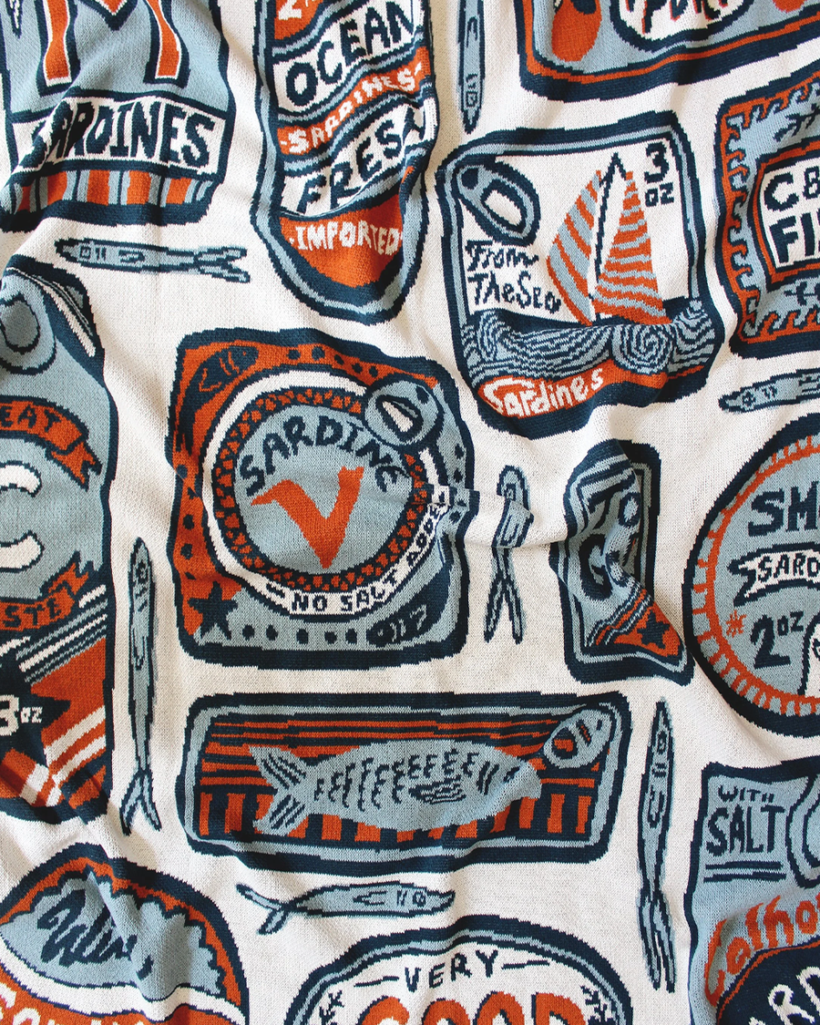 up close of white tea towel with orange and blue sardine can print