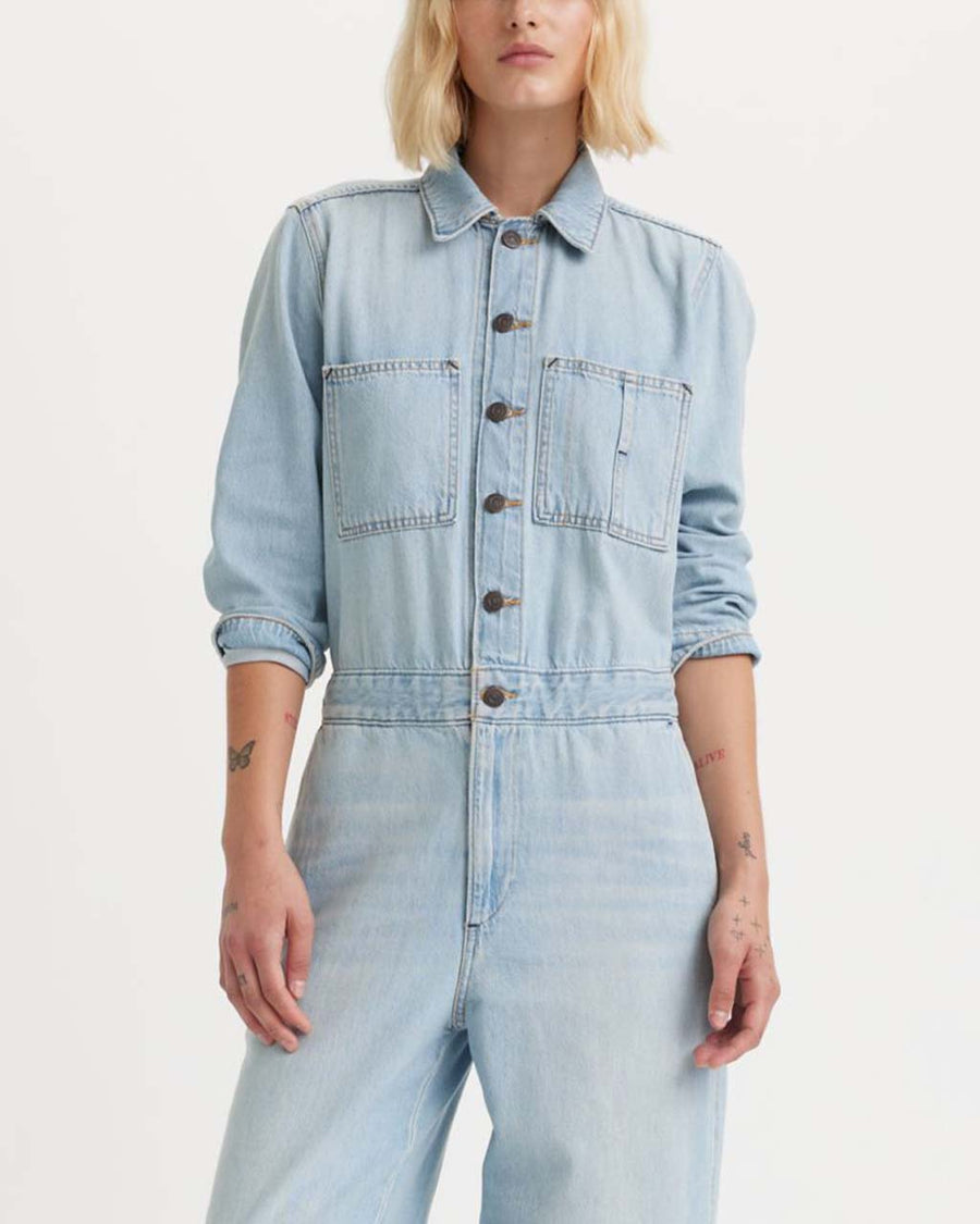 model wearing light denim jumpsuit with button front, patch pockets, collar and long sleeves