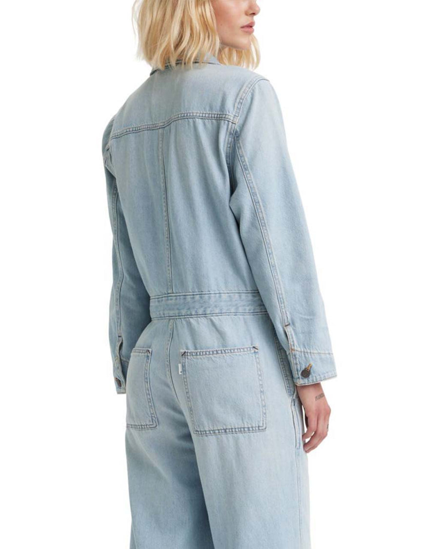 back view of model wearing light denim jumpsuit with button front, patch pockets, collar and long sleeves