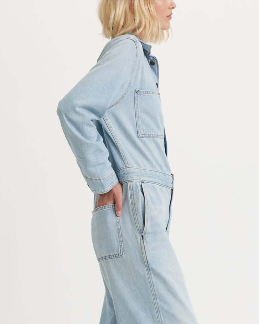 side view of model wearing light denim jumpsuit with button front, patch pockets, collar and long sleeves