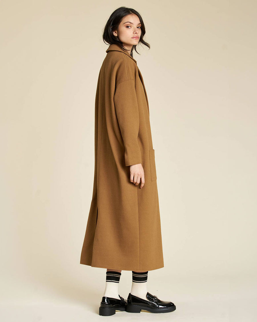 side view of model wearing brown wool midi length jacket with front patch pockets