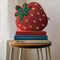 strawberry shaped beaded throw pillow on a stack of books