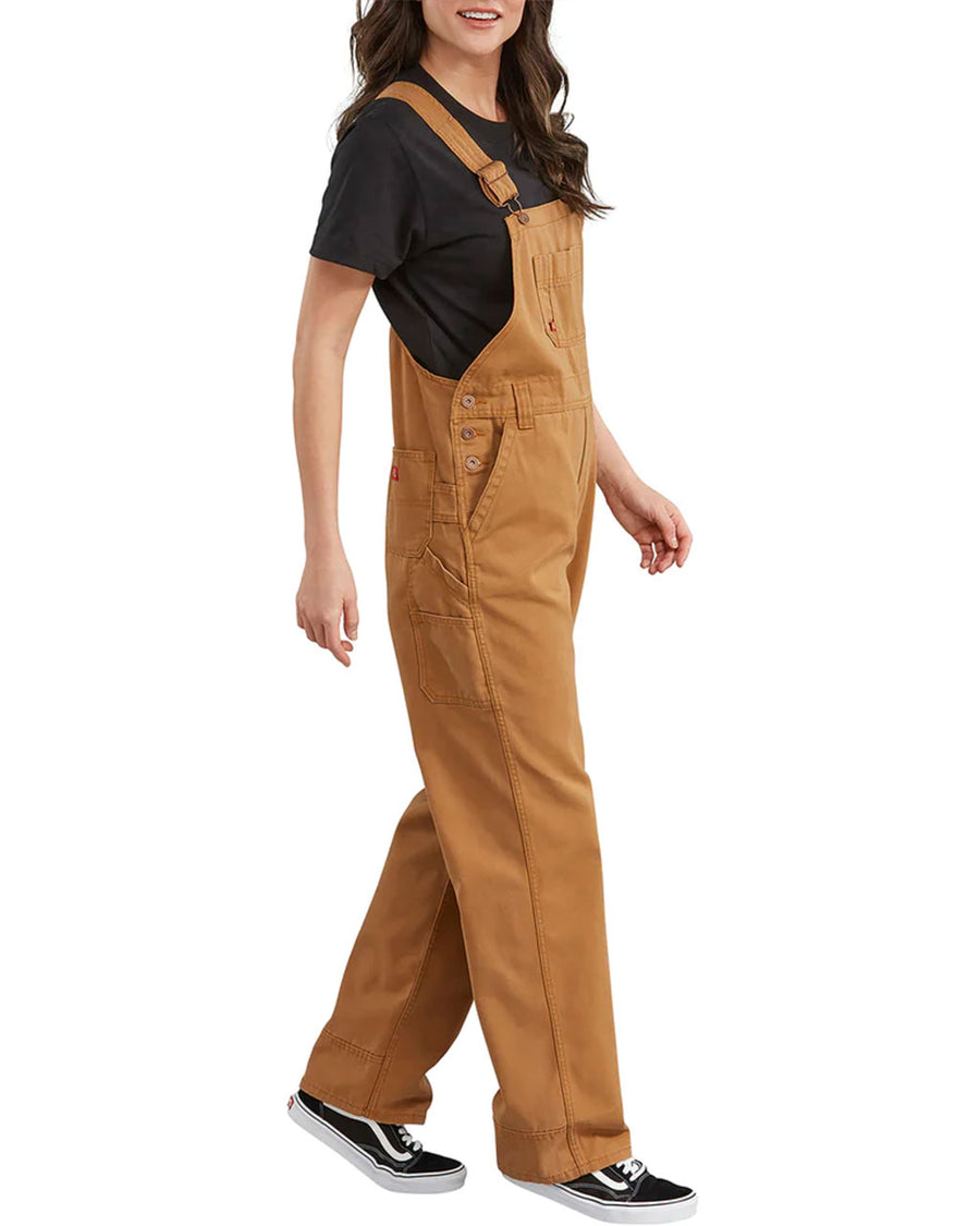side view of model wearing light brown cotton work overalls with front and slit pockets