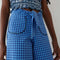 up close of model wearing blue gingham pants with patch pockets with dark blue trim and tie waist