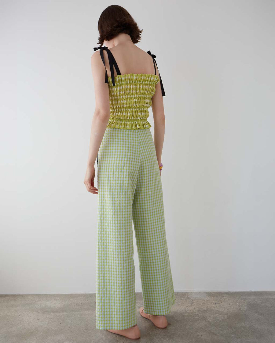 back view of model wearing green gingham pants with patch pockets with black trim and tie waist