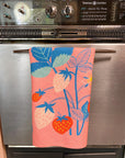 folded pink tea towel with colorful strawberry print hanging on an oven handle