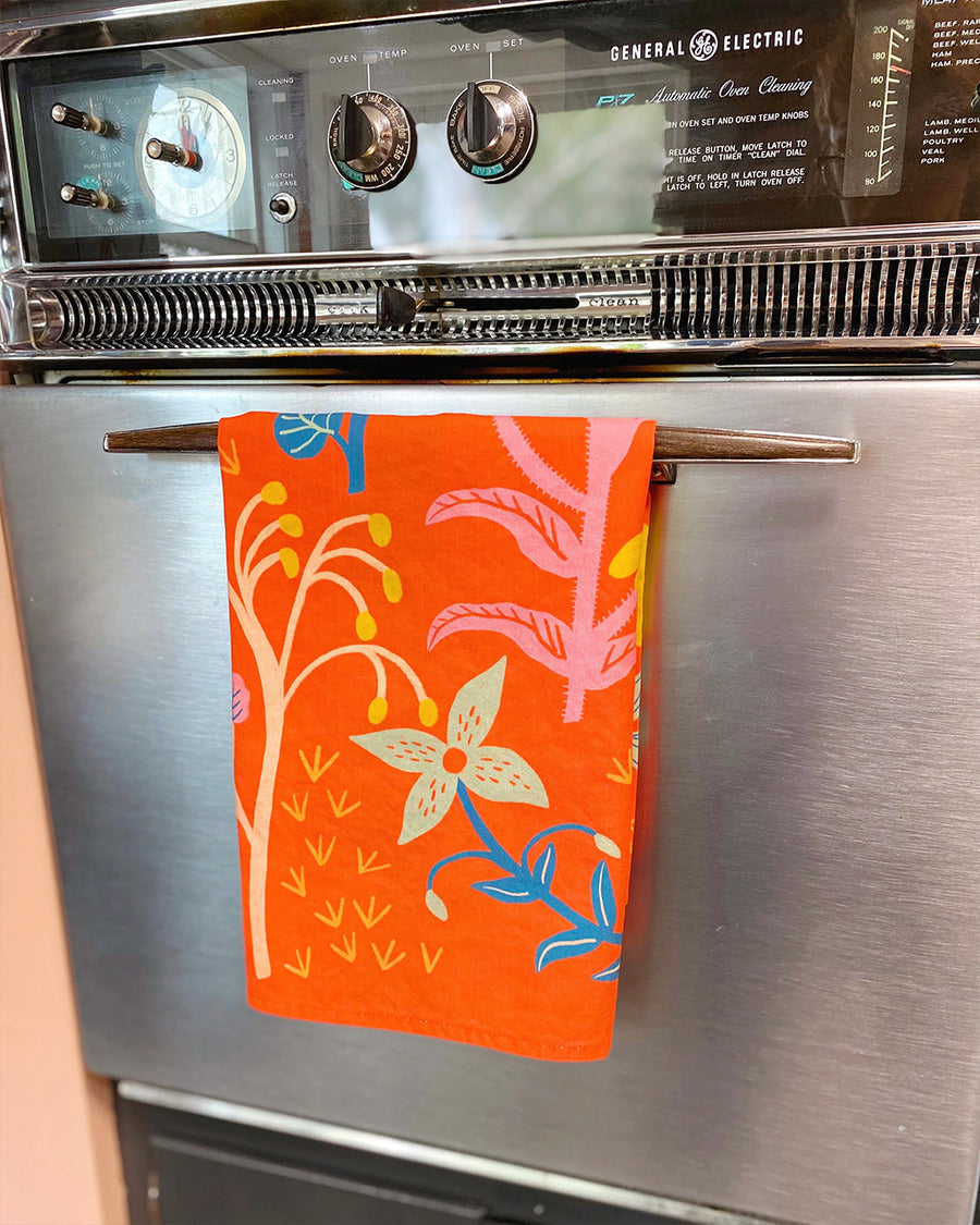 folded red tea towel with abstract wildflower print hanging on the oven handle