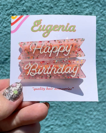 model holding pink glittery hair clips with white 'happy' and 'birthday' on them