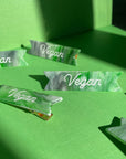 gold alligator clips on green and white hair clips with white 'vegan' across the front