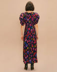 back view of model wearing black midi dress with front slit, shirred puff sleeves and colorful leopard print