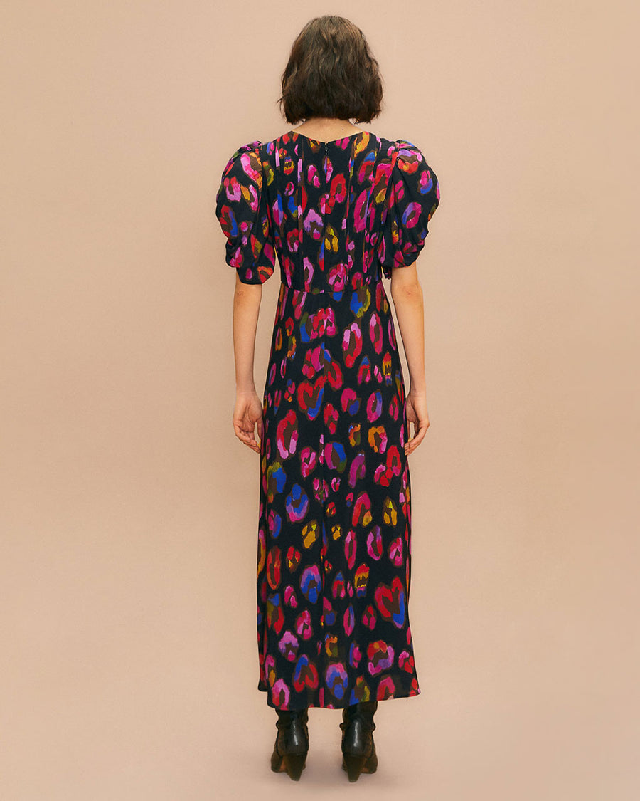 back view of model wearing black midi dress with front slit, shirred puff sleeves and colorful leopard print