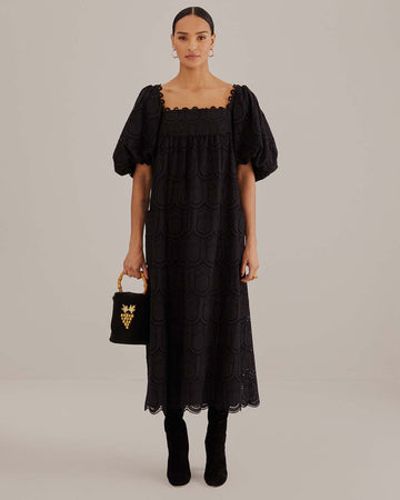 model wearing black eyelet maxi dress with empire waist, puff sleeves and scalloped hem
