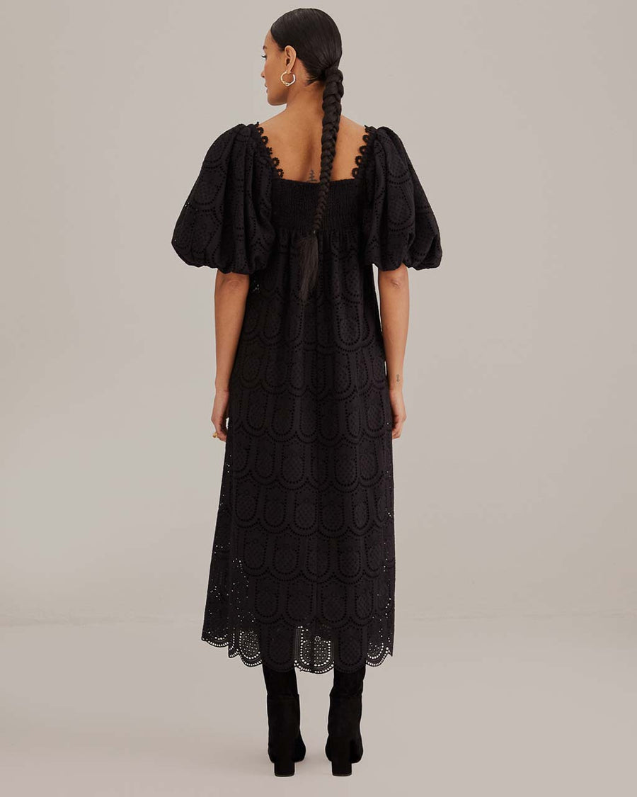 back view of model wearing black eyelet maxi dress with empire waist, puff sleeves and scalloped hem
