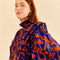 up close of model wearing cobalt blouse with high neck, ruffle sleeves, and all over orange and pink mushroom print