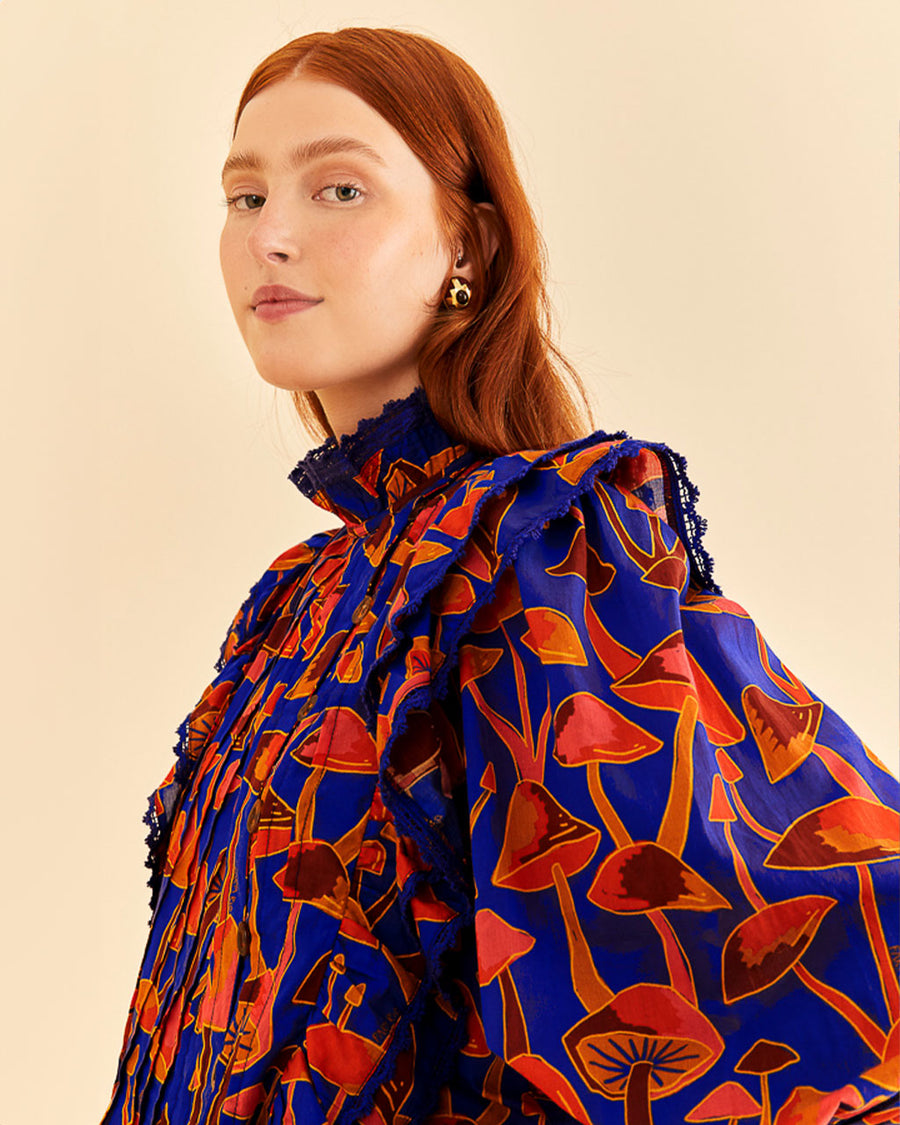up close of model wearing cobalt blouse with high neck, ruffle sleeves, and all over orange and pink mushroom print