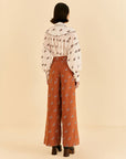 backview of model wearing orange high waisted pants with pleats, button front and all over horse print