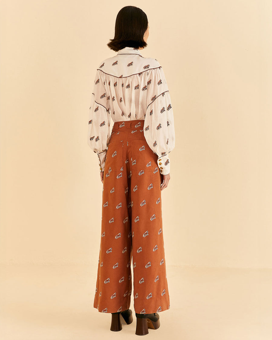backview of model wearing orange high waisted pants with pleats, button front and all over horse print