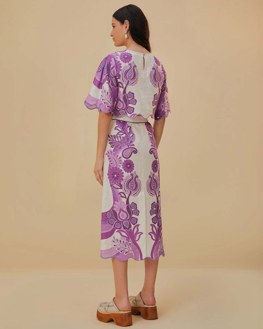 back view of model wearing white midi skirt with purple abstract floral and wavy hem and matching cropped blouse