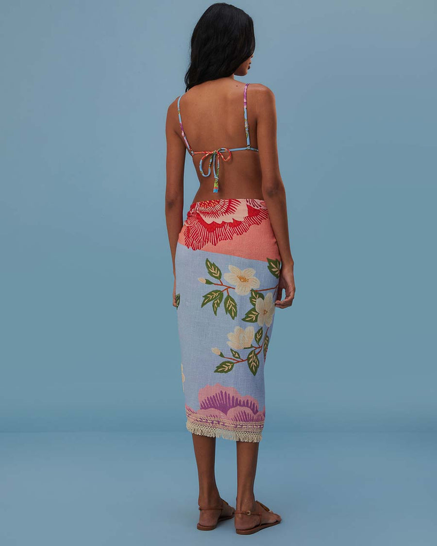 back view of model wearing blue sarong with abstract floral print with tan fringe on the end