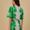 back view of model wearing white cropped blouse with green abstract floral print and wavy hems