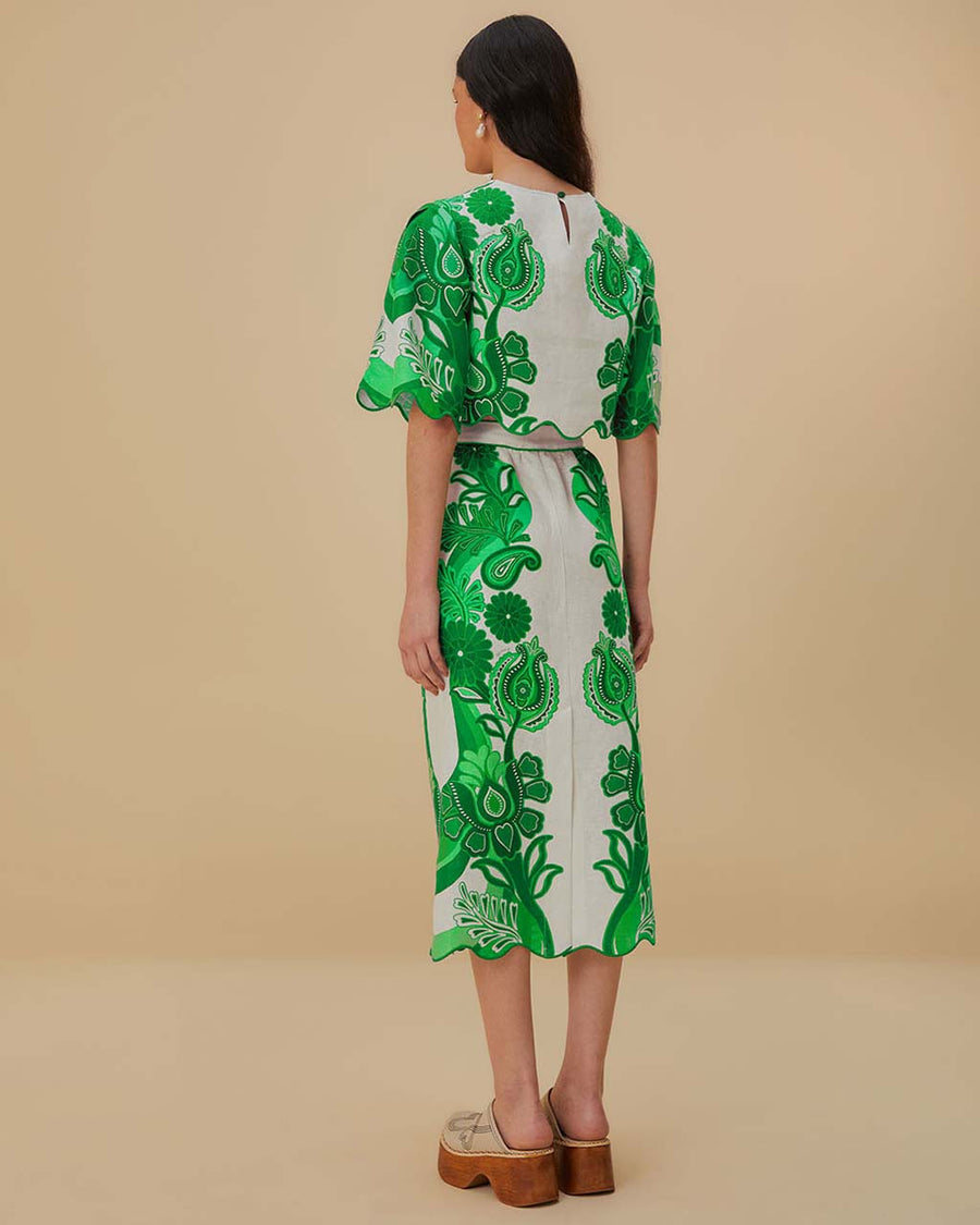 back view of model wearing white midi skirt with green abstract floral print and wavy hems and matching blouse