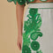 up close of model wearing white midi skirt with green abstract floral print and wavy hems and matching blouse
