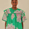 model wearing green flutter sleeve blouse with pink and white flowers, flutter sleeves and ric rac trim