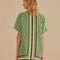 back view of model wearing green short sleeve bottom down top with pineapple print and green, cream and red stripes down the center