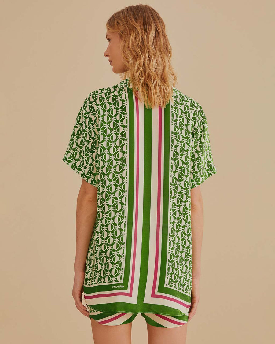 back view of model wearing green short sleeve bottom down top with pineapple print and green, cream and red stripes down the center