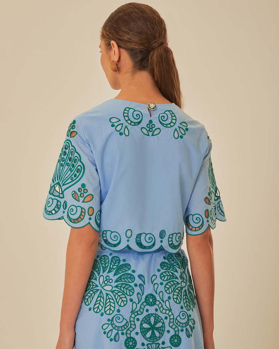 back view of model wearing. light blue cropped top with green cut out design and flutter sleeves